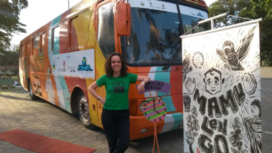 Mariane Gutierrez faz pose e sorri na frente de um ônibus colorido. É dentro deste ônibus que são realizadas as peças