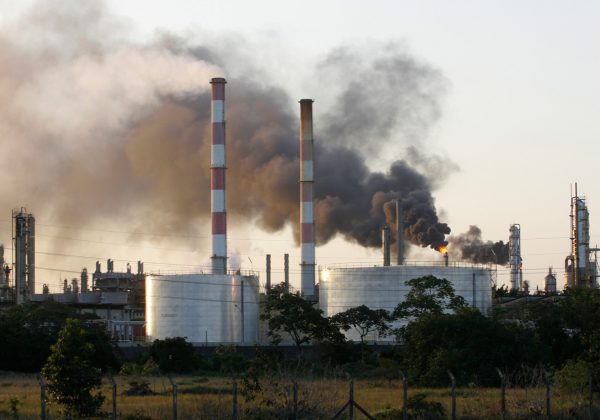 Foto de uma fábrica, contendo torres de resfriamento com fumaça preta saindo delas.