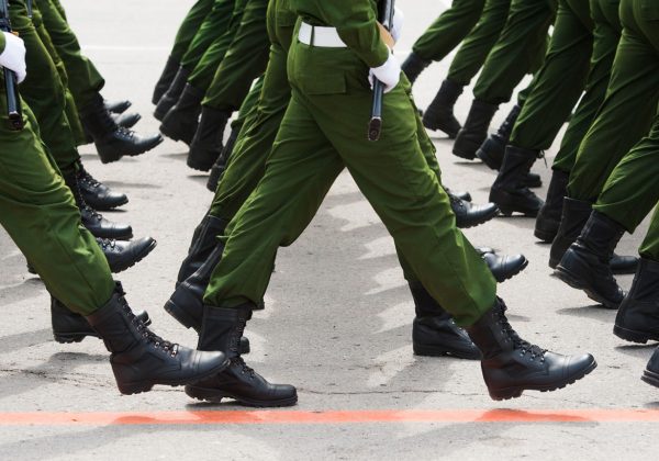 Foto das pernas de um batalhão marchando, todos usam calças verdes e botas pretas.