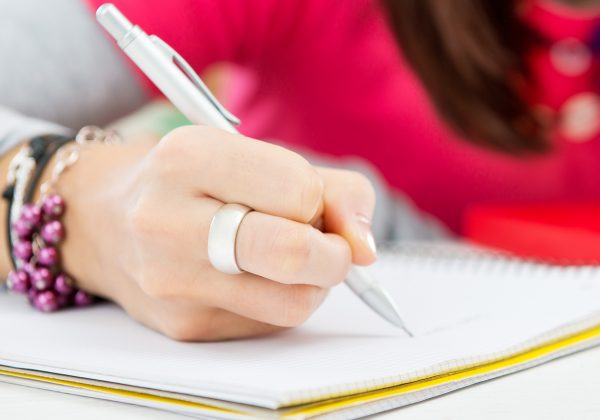 Foto em detalhe de mão escrevendo com uma lapiseira em um caderno